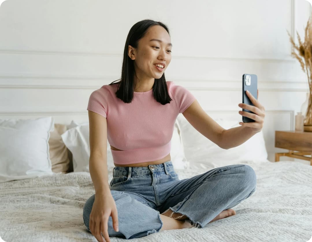 Woman sitting on bed taking a selfie with her phone